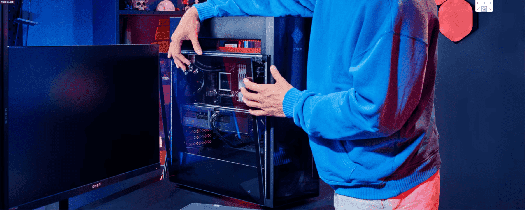 A person in a blue hoodie examining the internal components of an OMEN desktop PC with a transparent glass side panel illuminated by red and blue lighting