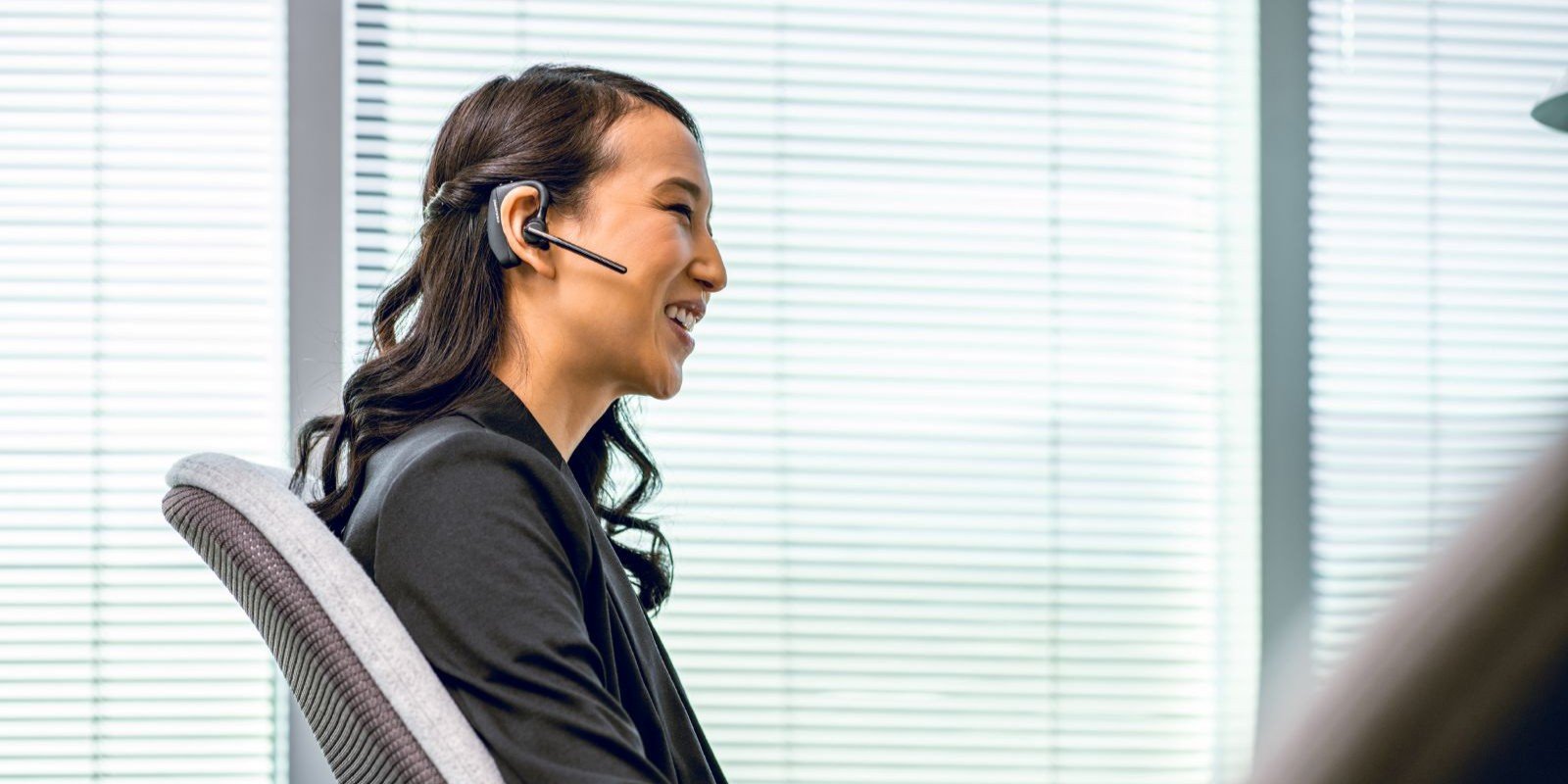 Smiling executive using Poly Voyager 5200 Bluetooth headphones during a video call in her officeRetryClaude can make mistakes. Please double-check responses